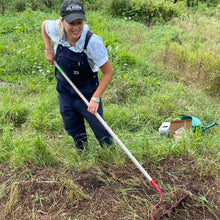Load image into Gallery viewer, Farmer in overalls using a rake to prepare the soil