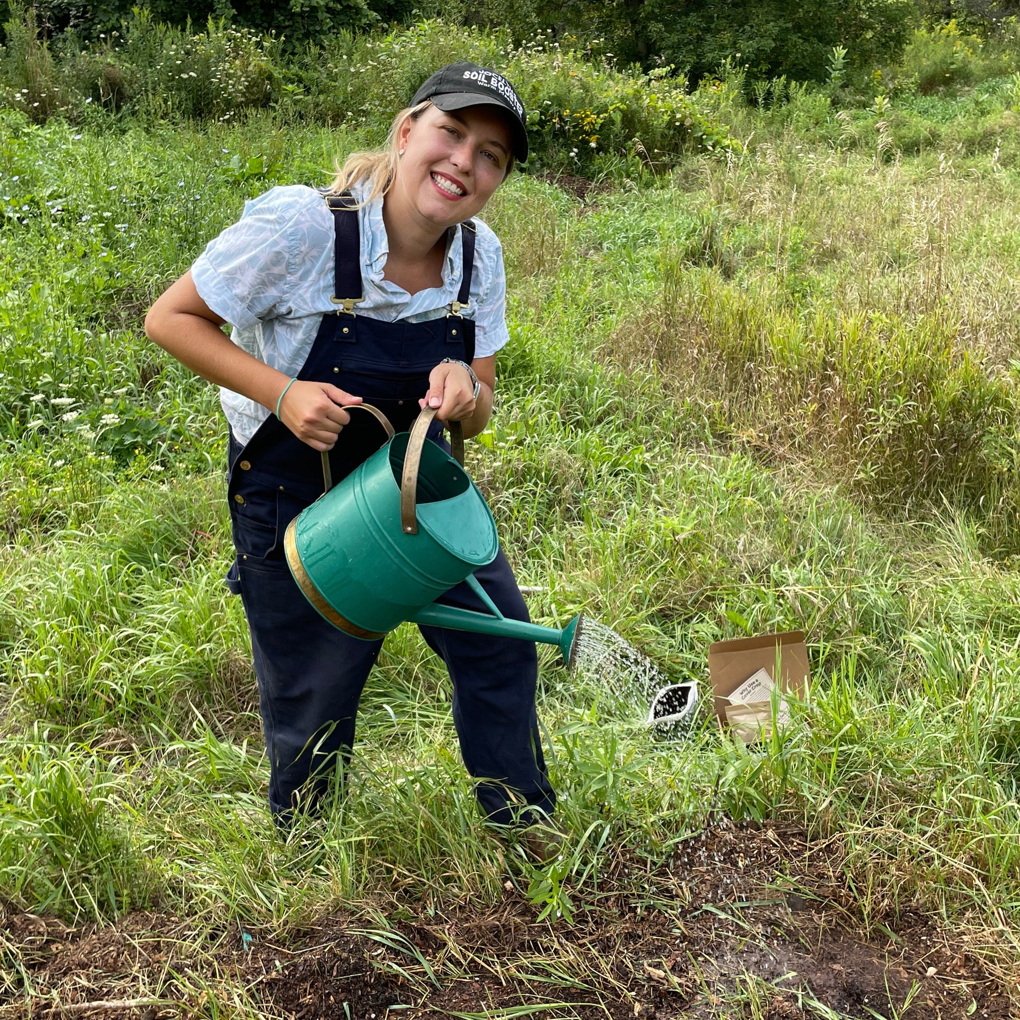 Female farmer in field smiling and holding a watering can